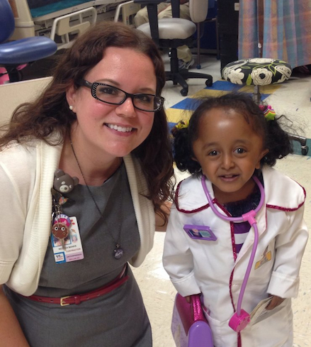 Rebeca sonriendo con su paciente que va vestida de Doc McStuffins con bata blanca y estetoscopio rosa
